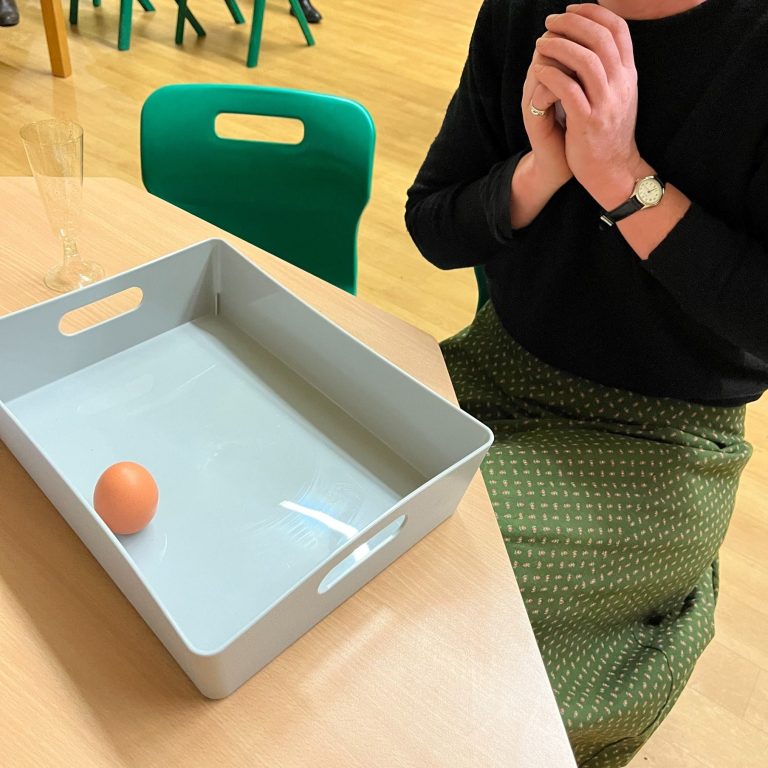 A photo of an egg balanced on its point. A torso can be seen in the picture (face not included for privacy) with hands together pleased.